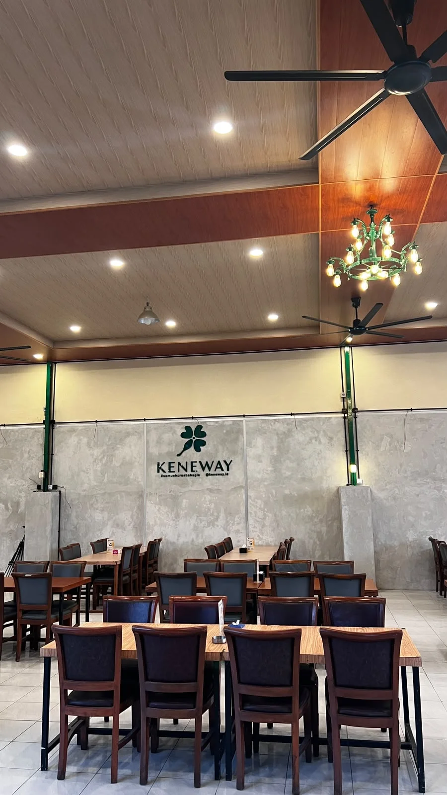 Area meja dan kursi KENEWAY dengan logo clover di dinding dan lampu gantung hijau
