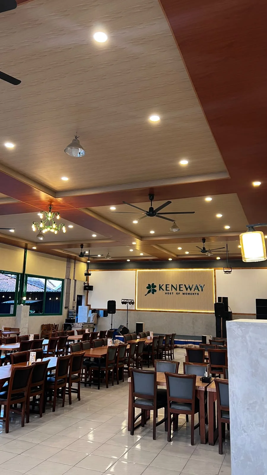Suasana ruang makan KENEWAY dengan meja kayu, jendela hijau, dan lampu gantung